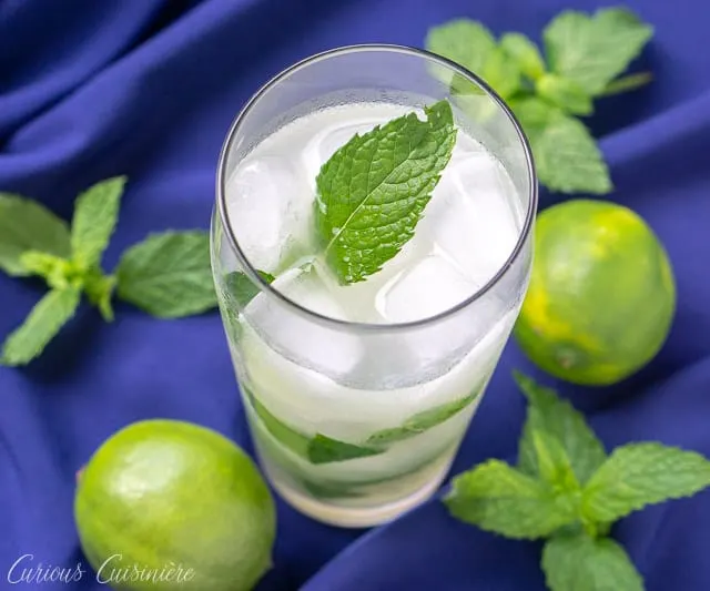 Cuban mojito beverage on a blue background with limes and fresh mint leaves. mint, lime and white rum. | www.CuriousCuisiniere.com 