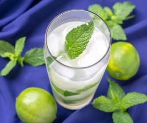 Cuban mojito beverage on a blue background with limes and fresh mint leaves. mint, lime and white rum. | www.CuriousCuisiniere.com
