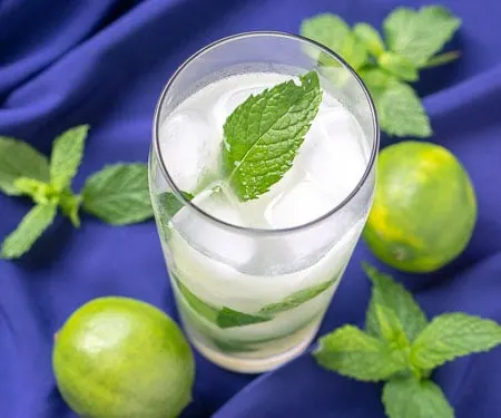 Cuban mojito beverage on a blue background with limes and fresh mint leaves. mint, lime and white rum. | www.CuriousCuisiniere.com