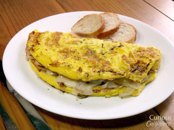 Fluffy eggs are filled with flavorful caramelized onions and sharp Swiss cheese in an omelette inspired by the flavors of French onion soup. | www.CuriousCuisiniere.com
