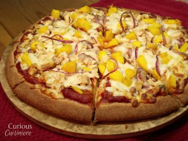 This Mango BBQ Chicken Pizza combines a sweet mango barbecue sauce with chicken and the unlikely sweet pizza topping of fresh mangoes for one delicious pizza that reminds us of a summer barbecue.   | Curious Cuisiniere