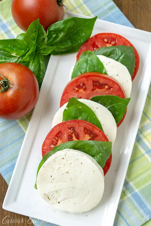 A traditional Italian appetizer Insalata Caprese (or Caprese Salad) with fresh mozzarella, juicy tomatoes, and bright basil. A perfect summer salad. | www.CuriousCuisiniere.com 