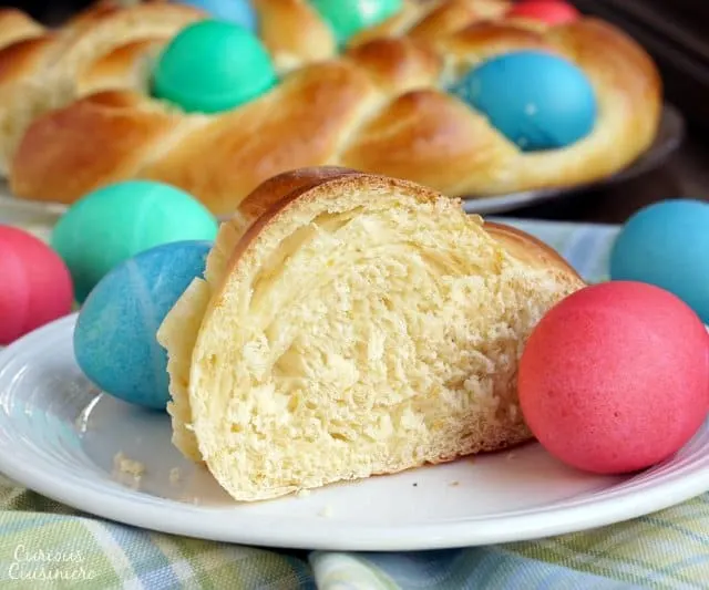 A slice of Italian Easter Bread, Pane di Pasqua, surrounded by dyed Easter eggs. | www.CuriousCuisiniere.com