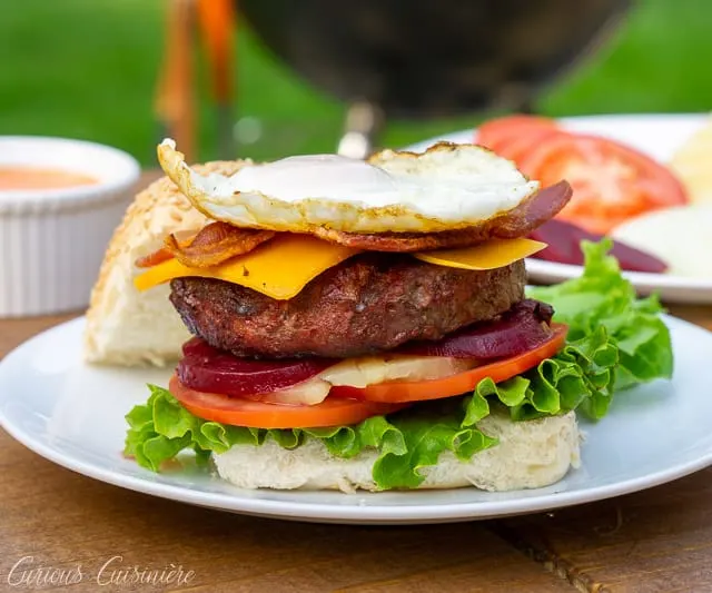 This loaded Australian Hamburger is a mile-high burger with egg, bacon, cheddar cheese, pineapple, pickled beets, sweet onion, lettuce, tomato, and a chili mayo sauce. If you love burger toppings, this Aussie Burger is for you! | www.CuriousCuisiniere.com