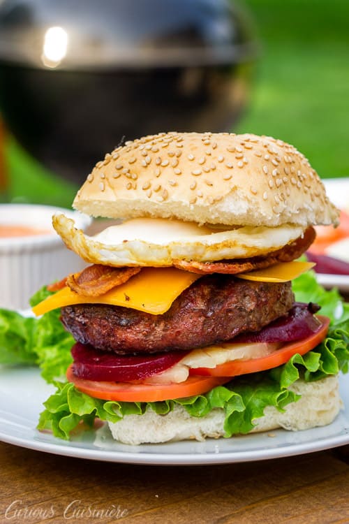 This loaded Australian Hamburger is a mile-high burger with egg, bacon, cheddar cheese, pineapple, pickled beets, sweet onion, lettuce, tomato, and a chili mayo sauce. If you love burger toppings, this Aussie Burger is for you! | www.CuriousCuisiniere.com