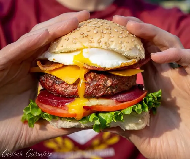 This loaded Australian Hamburger is a mile-high burger with egg, bacon, cheddar cheese, pineapple, pickled beets, sweet onion, lettuce, tomato, and a chili mayo sauce. If you love burger toppings, this Aussie Burger is for you! | www.CuriousCuisiniere.com