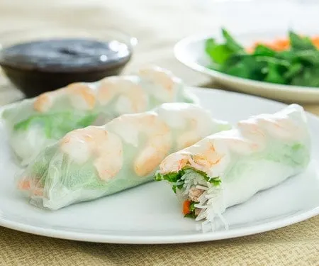 Three Vietnamese spring rolls with shrimp and greens on a white plate.