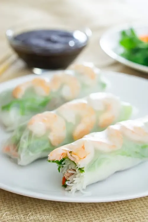 Three Vietnamese spring rolls with shrimp and greens on a white plate. With hoisin sauce for dipping.
