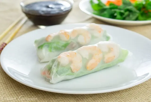 Two Vietnamese spring rolls with shrimp and greens on a white plate.