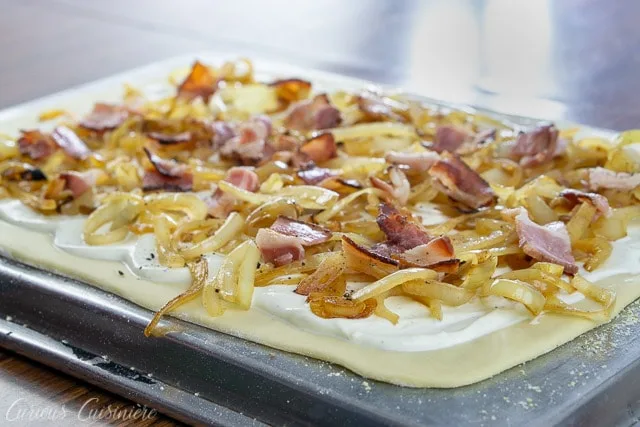 Layering bacon, caramelized onions, and creme fraiche on a thin crust for a classic German Flammkuchen recipe.