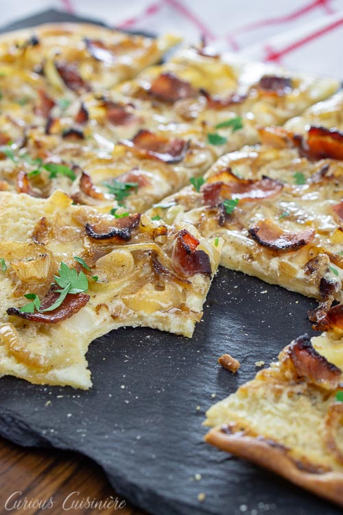 Flammekuchen, German pizza, with a bite taken out on a slate board.