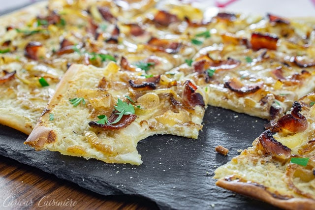 Flammekuchen, German pizza, with a bite taken out on a slate board.