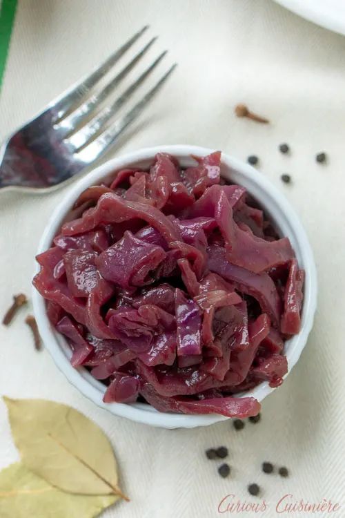Overhead shot of Blaukraut, German Red Cabbage, in a small bowl with bay leaves and allspice berries. 