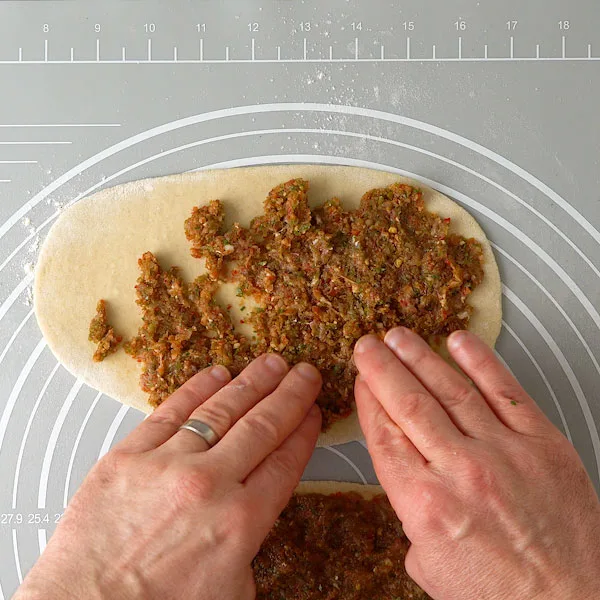 Spreading the meat and vegetable mixture on lahmacun for Turkish pizza