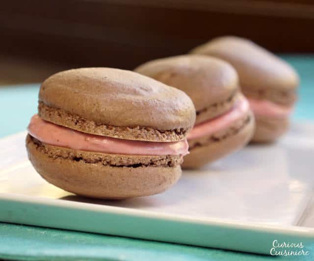 These Chocolate French Macarons combine a soft and fudgy macaron cookie with a raspberry filling for a perfectly delightful combo. | www.CuriousCuisiniere.com