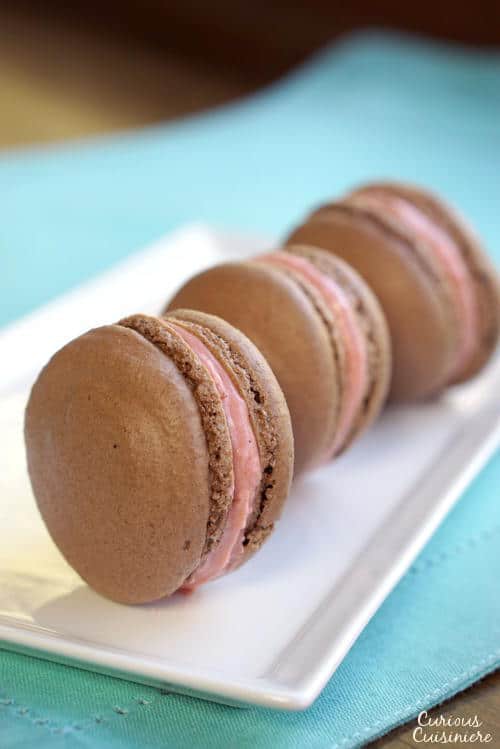 These Chocolate French Macarons combine a soft and fudgy macaron cookie with a raspberry filling for a perfectly delightful combo. | www.CuriousCuisiniere.com