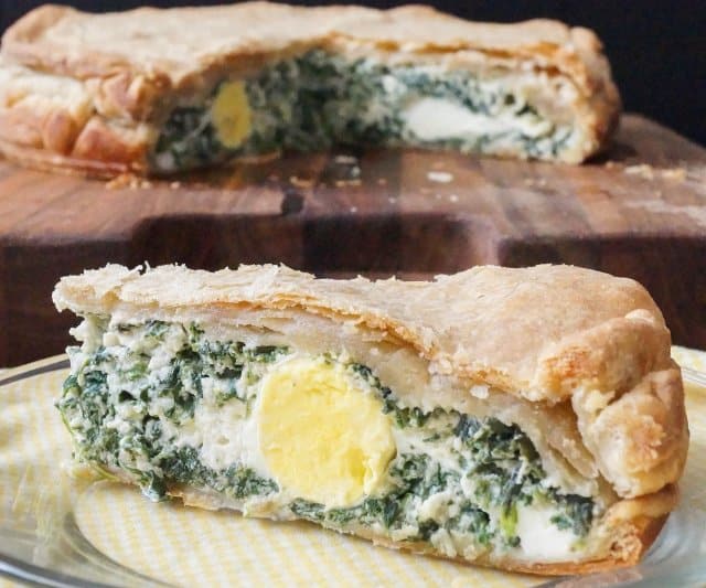 Torta Pasqualina is a savory Italian pie filled with greens and ricotta cheese that is traditionally enjoyed for Easter. Image of cut pie with greens and hard cooked egg showing in the slice.