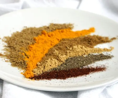 Warm ground spices arranged on a white plate. High angle.