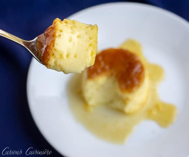 A bite of Spanish egg flan hovering over a plate of flan.  | www.CuriousCuisiniere.com