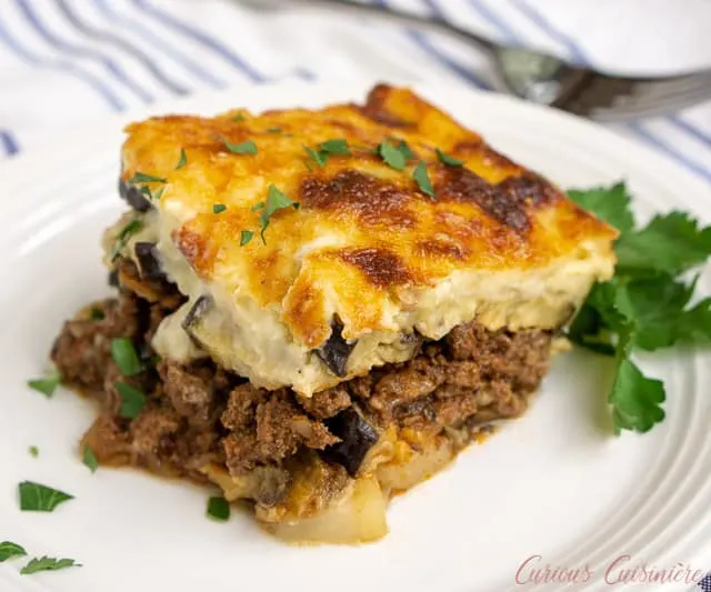 Greek Moussaka is an eggplant casserole filled with layers of eggplant and a warmly spiced meat sauce, all covered in a rich béchamel sauce. This is a recipe for some serious Greek comfort food! | www.CuriousCuisiniere.com
