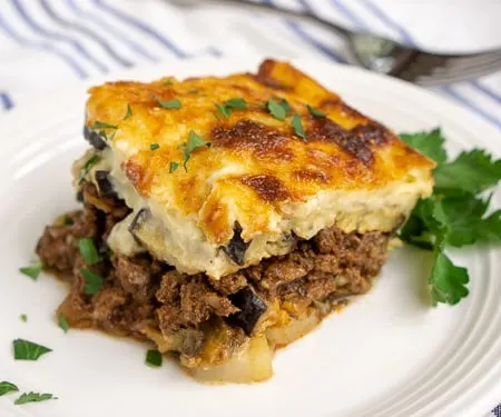 Greek Moussaka is an eggplant casserole filled with layers of eggplant and a warmly spiced meat sauce, all covered in a rich béchamel sauce. This is a recipe for some serious Greek comfort food! | www.CuriousCuisiniere.com