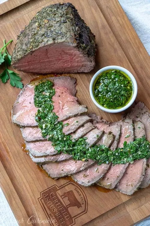 Top down view of a top round roast sliced with chimichurri sauce. | www.CuriousCuisiniere.com