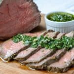 Horizontal shot of a chimichurri marinated top round beef roast. Served with a side of chimichurri.