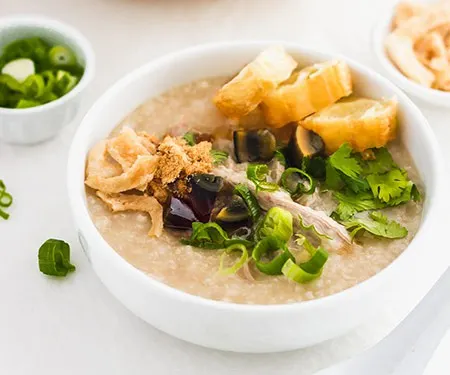 Preserved century egg congee with green onions and fried yu tiao Chinese donuts. | www.CuriousCuisiniere.com