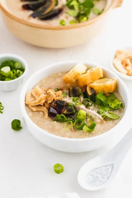 Preserved century egg congee with green onions and fried yu tiao Chinese donuts. | www.CuriousCuisiniere.com 