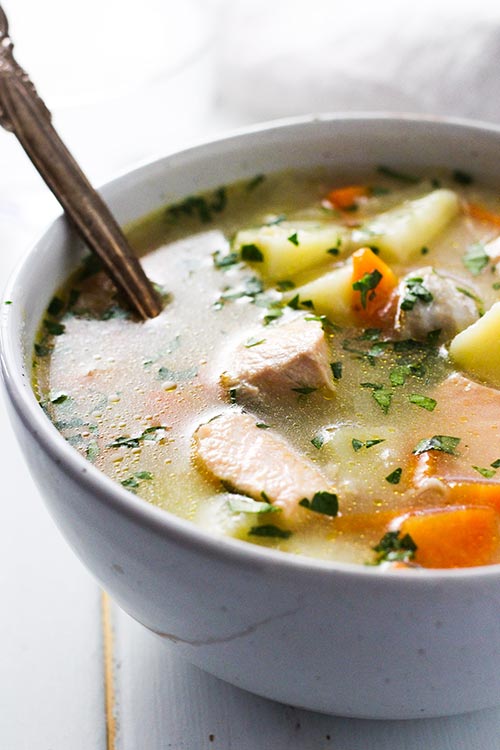 een kom Ukha, Russische vissoep met een rustieke lepel. Vis wordt zachtjes gekookt met aardappelen en wortelen in een rijke bouillon gekruid met baai en zwarte peper. | www.CuriousCuisiniere.com 