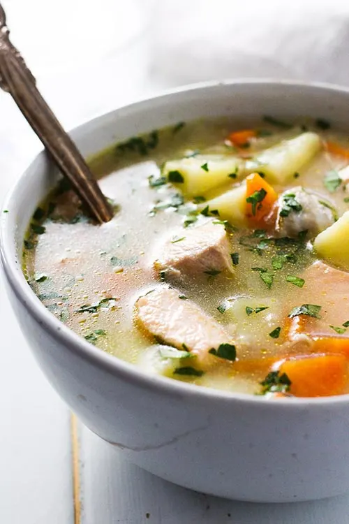 A bowl of Ukha, Russian fish soup with a rustic spoon. Fish is gently cooked with potatoes and carrots in a rich broth seasoned with bay and black pepper. | www.CuriousCuisiniere.com 