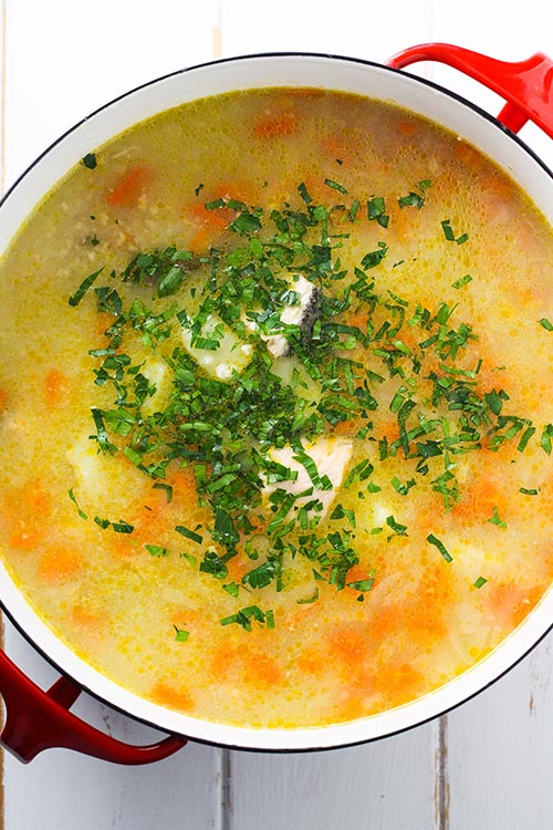 Draufsicht auf einen Topf Ukha, russische Fischsuppe. Fisch wird sanft mit Kartoffeln und Karotten in einer reichen Brühe mit Lorbeer und schwarzem Pfeffer gewürzt gekocht. | www.CuriousCuisiniere.com 