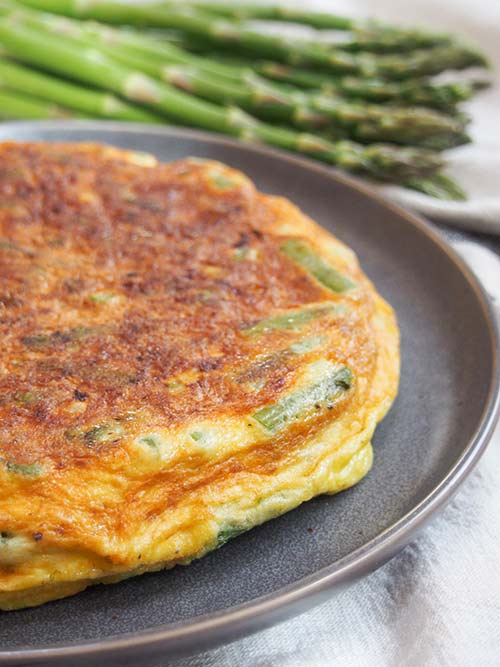 Plated Italian asparagus fritatta on a black plate, before cutting.