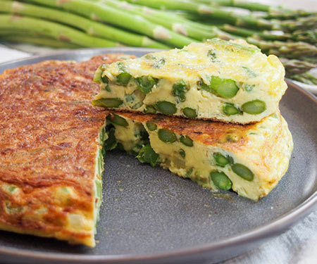 Asparagus fritatta, cut and plated with asparagus in the background.
