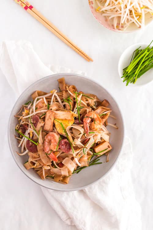 Malaysian Stir Fried Rice Noodles - Char Kway Teow - in a large white bowl with Chinese sausage (lap cheong)