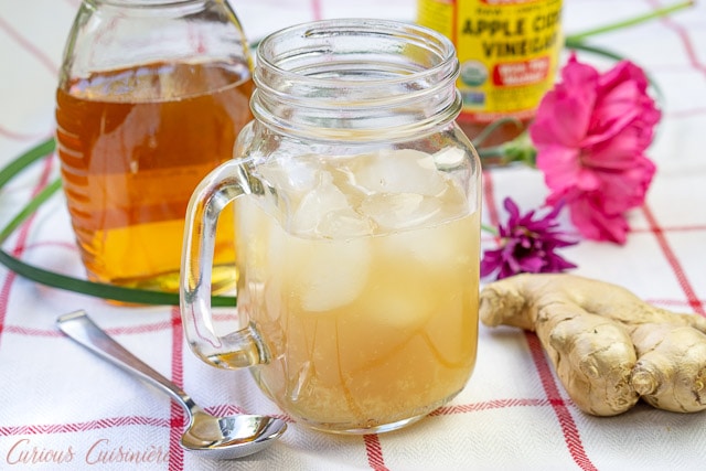 Carribean Switchel - Honey Ginger Drink - in a handled glass mug surrounded by a jar of honey and a piece of ginger