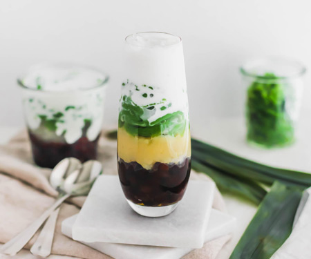 Top view of cendol, Malaysian pandan jellies, layered with red azuki beans, yellow mung beans, and coconut milk in a glass.