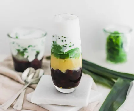 Top view of cendol, Malaysian pandan jellies, layered with red azuki beans, yellow mung beans, and coconut milk in a glass.