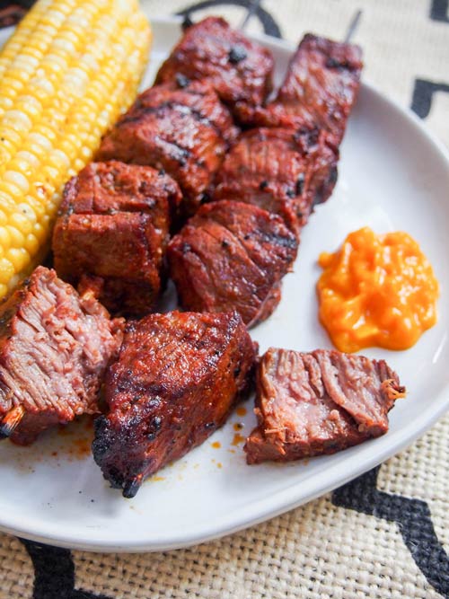 Anticuchos, Peruaanse gegrilde runderspiesjes op een bord met maïs en saus, gesneden om de sappige textuur van het vlees te laten zien.