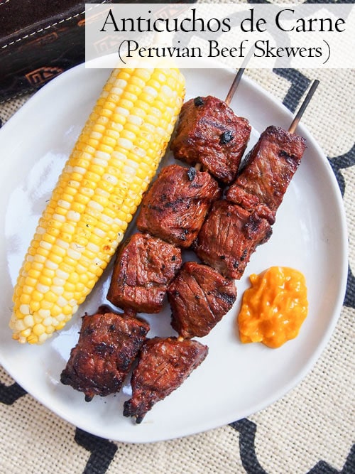 Overhead bild av Anticuchos, peruanska grillade nötköttspett på en tallrik med majs och sås