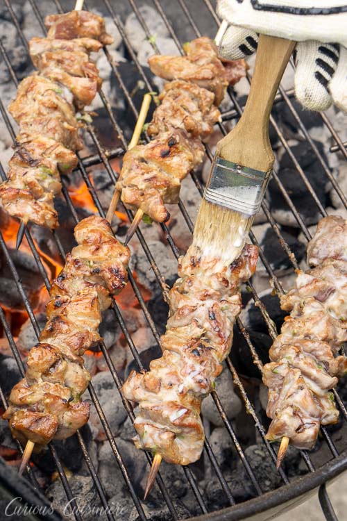 Pork skewers on the grill being brushed with coconut milk