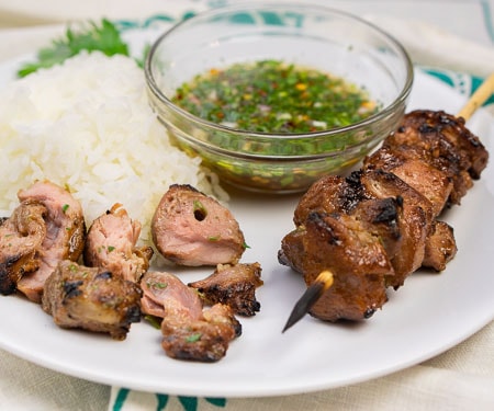 Thai pork kabobs with rice and dipping sauce with pieces taken from the skewer - cropped image