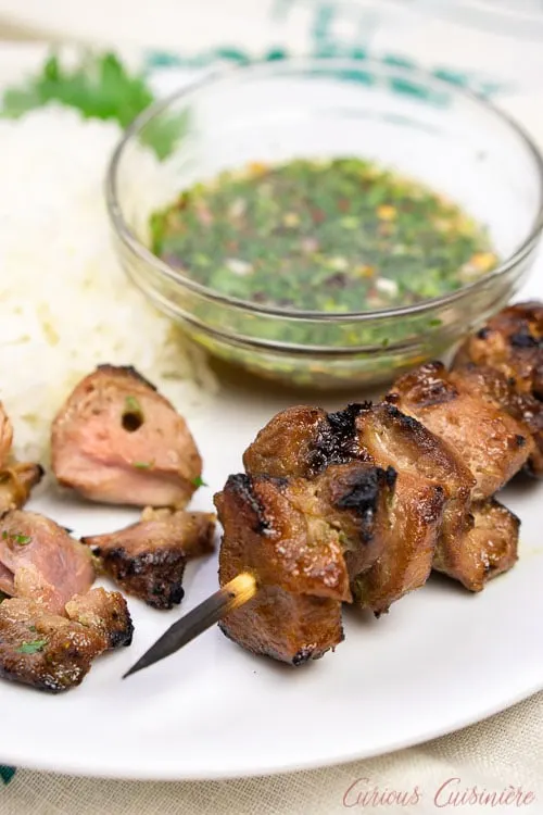 Thai pork kabobs with rice and dipping sauce with pieces taken from the skewer - vertical image