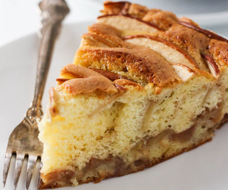 Close up of a slice of sharlotka, Russian apple cake on a white plate with a vintage fork.