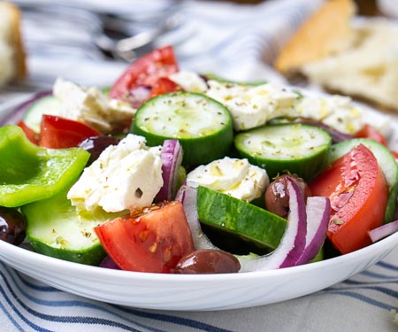 Close up of a bowl of authentic Greek salad (Horiatiki), a chunky salad without lettuce. Summer vegetables, salty olives, and creamy feta cheese.