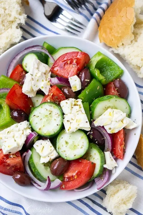 Overheat image of a traditional Greek salad (Horiatiki) is a chunky salad that combines fresh summer produce, salty olives, and creamy goat cheese with a light oil and vinegar dressing.
