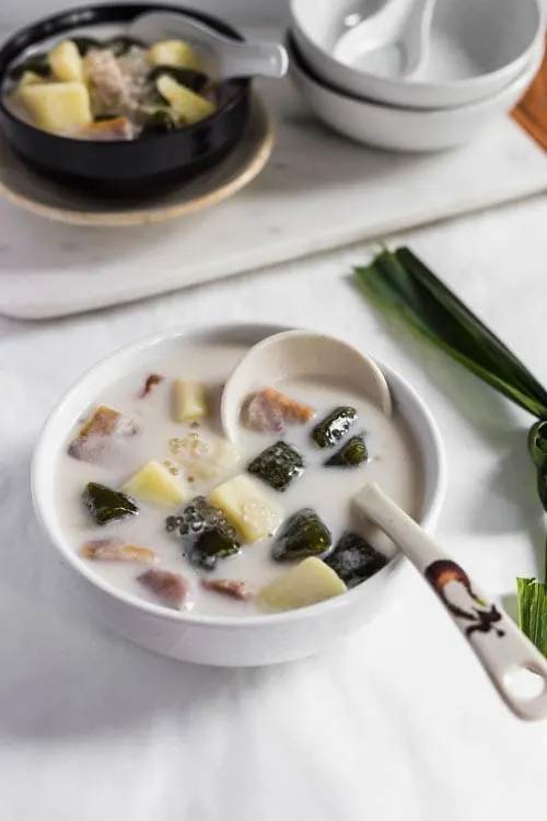 Bubur Cha Cha, a creamy and sweet Malaysian dessert made from yam, taro, and coconut milk in a white bowl with a pandan leaf. 
