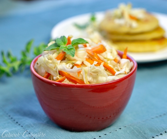 El Salvadoran Curdito pickled cabbage and carrot slaw with pupusas in the background