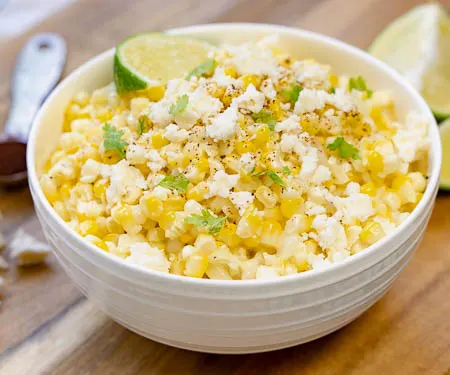 A bowl of Esquites Mexican street corn salad topped with a lime wedge and queso fresco cheese and chili powder