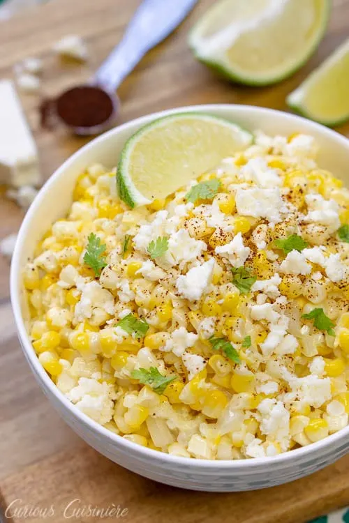 A bowl of Esquites Mexican street corn salad topped with a lime wedge and queso fresco cheese